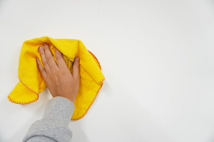 En mans hand som torkar av en vägg med en gul trasa för att få bort smuts