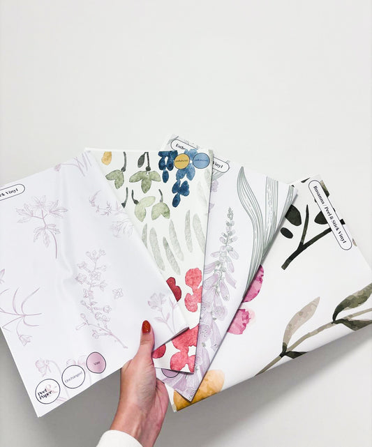 En kvinnohand som håller tapetprov med blommiga designer från Peel & Paper