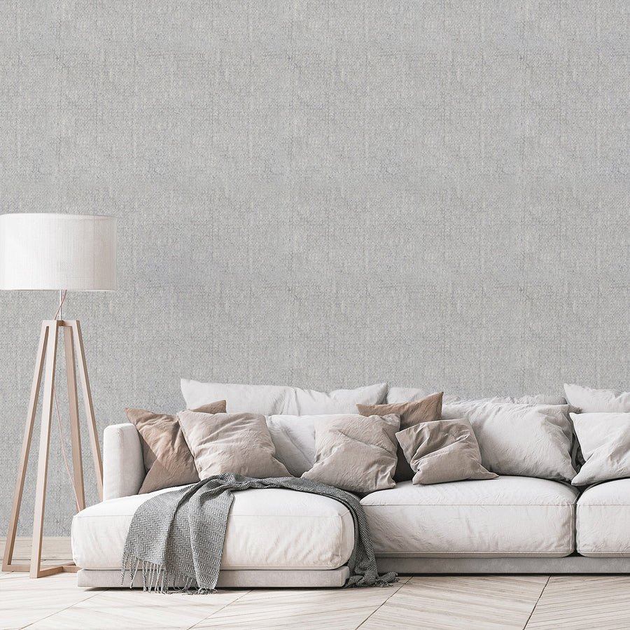 Ett vardagsrum med en golvlampa och en vit tygsoffa, med tapeten 'Alina', en grå tapet med mjuk ulltygseffekt, vävt utseende och subtil tonvariation i en minimalistisk, upprepande design.