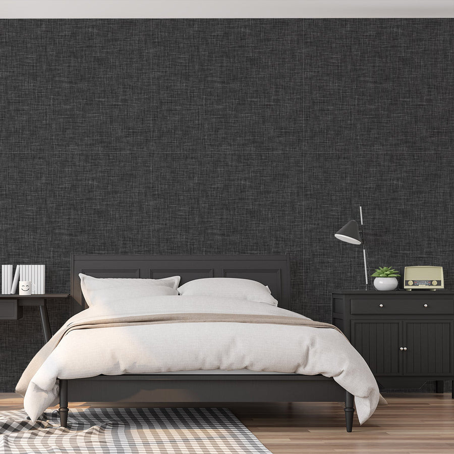 Ett sovrum med mörk sängram och sängbord, med tapeten 'Ashlyn', en mörkgrå tapet med subtil linnestruktur, vävt utseende och mjuk tonvariation i en minimalistisk design.