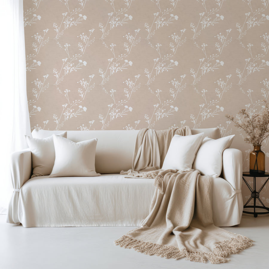 Ett vardagsrum med en soffa i linnetyg med kuddar och filtar och Daniella, en minimalistisk botanisk tapet med sköra vildblomsstänglar och smala lummiga grenar på en strukturerad neutral bakgrund i ett diskret upprepat mönster.