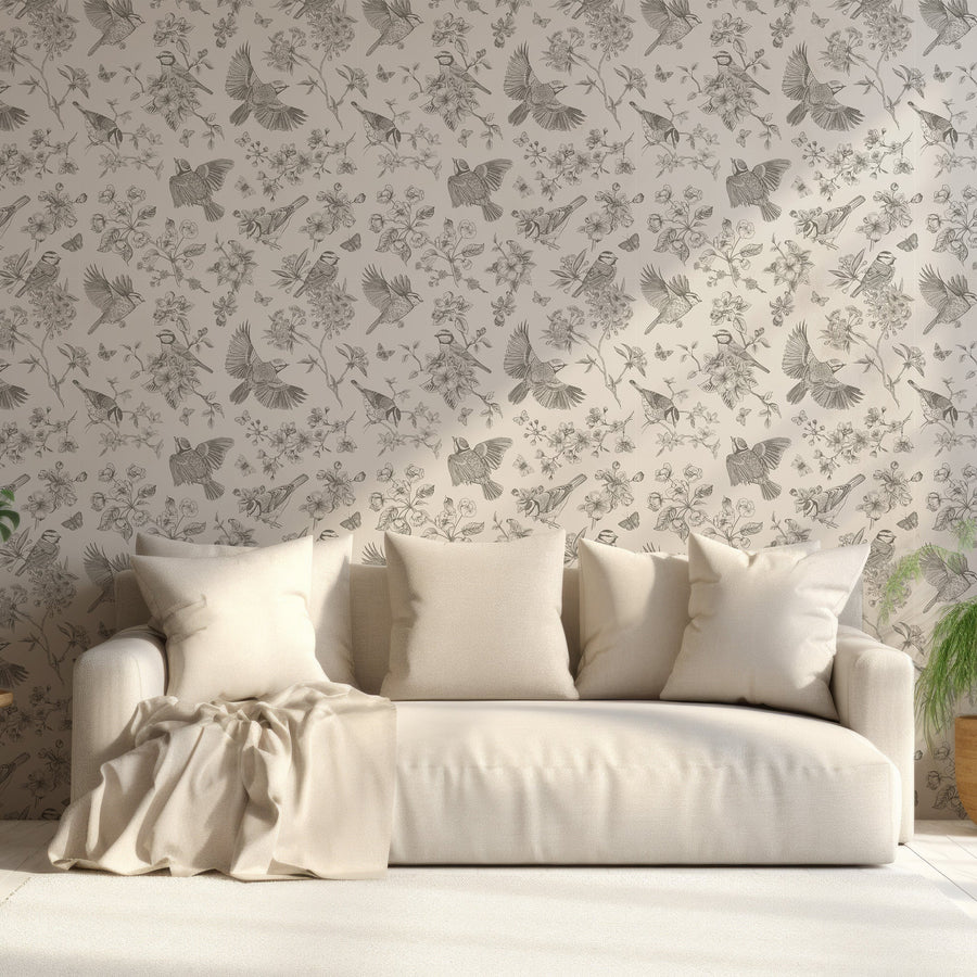 Ett vardagsrum med en krämvit soffa och tapeten Gianna, en beige tapet med fåglar, fjärilar, blommor och lummiga grenar i vintagestil i ett elegant, upprepande botaniskt mönster.