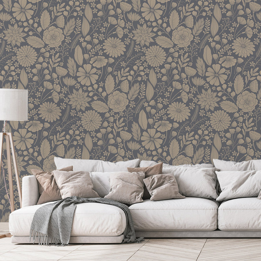 Ett vardagsrum med en beige soffa full av kuddar och en lampa, med tapeten 'Jessamine', en blå botanisk tapet med ömtåliga blommor, lummiga växter och fina botaniska illustrationer mot en mörkt blågrå bakgrund i ett upprepande mönster.