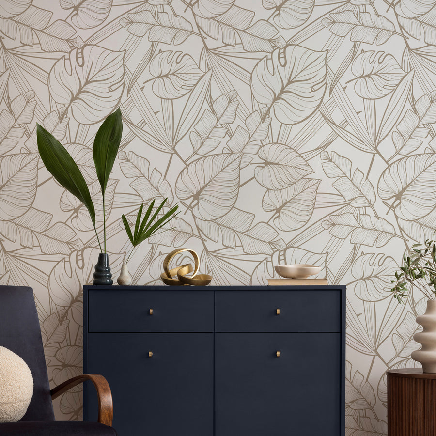 Ett vardagsrum med ett marinblått sideboard och tapeten 'Juniper Neutral', en vit tapet med ömtåliga guldfärgade konturer av tropiska blad i ett upprepande botaniskt mönster med modern, minimalistisk design.