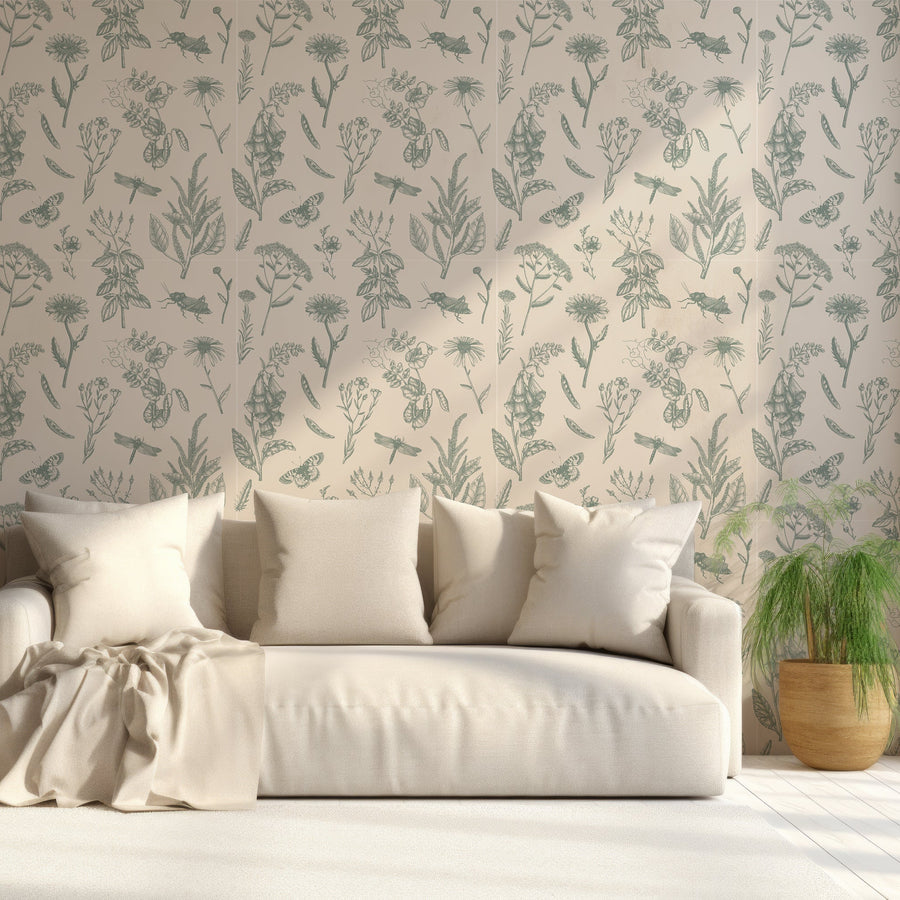 Ett vardagsrum med en krämvit soffa full av kuddar bredvid en liten grön växt, med tapeten 'Lillian', en grön botanisk tapet med ömtåliga fingerborgsblommor, vita prästkragar, lummiga växter och fjärilar mot en mjukt krämvit bakgrund i ett vintageinspirerat, upprepande mönster.