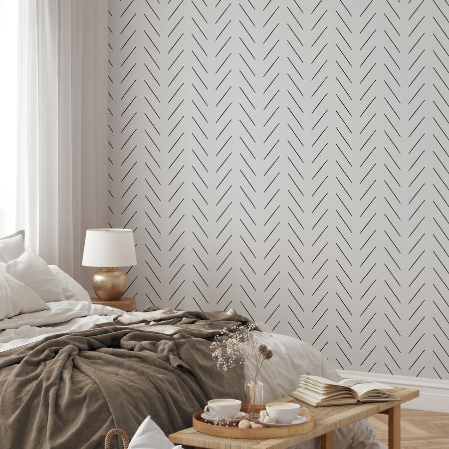 Ett avslappnat inrett sovrum som visar tapeten Livia, en monokrom tapet med ett minimalistiskt fiskbensmönster av tunna diagonala linjer i en upprepad geometrisk design.