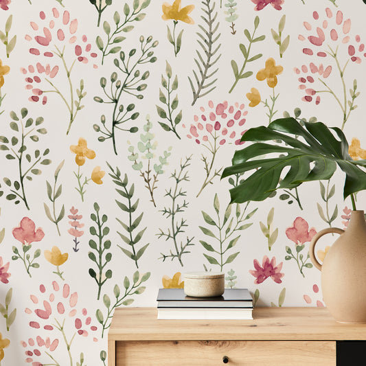 Ett vardagsrum med ett sideboard och tapeten 'Rosanna', en akvarelltapet med ömtåliga blommor och lummiga växter i mjuka gröna, gula och rosa toner mot en beige bakgrund i ett livfullt, upprepande botaniskt mönster.