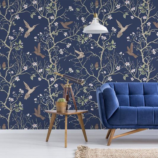 Ett vardagsrum med en blå capitonnésoffa och ett litet sidobord, med tapeten 'Denora', en mörk marinblå tapet med handritade chinoiserieträd, fåglar och färgglada blommor i ett elegant, upprepande botaniskt mönster.