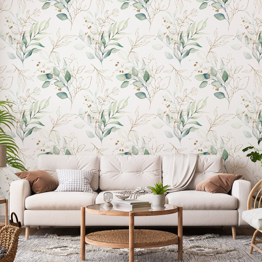 Ett vardagsrum med en krämvit soffa och tapeten Eucalyptus, en grön tapet med ömtåliga eukalyptusblad och guldfärgade linjeillustrationer i ett mjukt, upprepande botaniskt mönster.