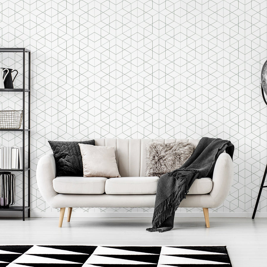 Ett vardagsrum med en krämvit tvåsitssoffa bredvid en svart metallhylla och en golvlampa, med tapeten 'Rosamund', en mörkgrön geometrisk tapet med överlappande romber och fina linjedetaljer i ett modernt upprepat mönster.