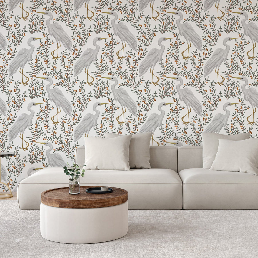 Ett vardagsrum med en vit soffa och ett soffbord, med tapeten Tallulah, en botanisk tapet med illustrerade hägrar, lummiga grenar och bär mot en ljus bakgrund i en vintageinspirerad upprepad design.